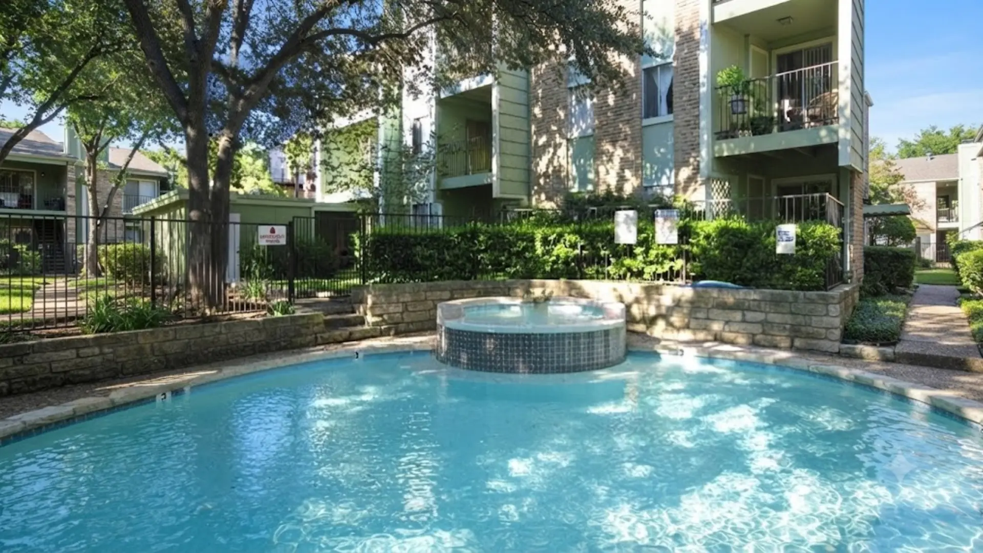 Outdoor swimming pool and elevated round hot tub spa surrounded by stone landscaping and apartment complex balconies.